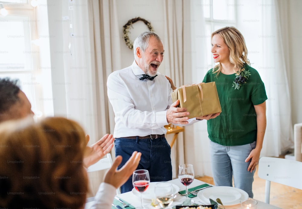 Beautiful young woman giving a gift to her father or grandfather on indoor party.