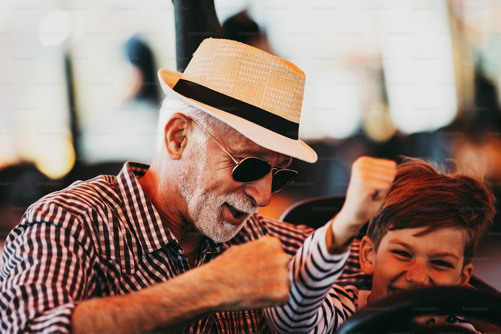 Abuelo y nieto divirtiéndose y pasando tiempo de buena calidad juntos en el parque de atracciones. Disfrutan y sonríen mientras conducen juntos un auto chocador.