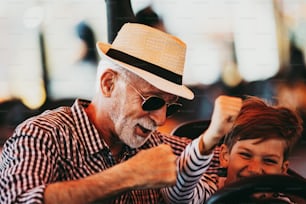 Grandfather and grandson having fun and spending good quality time together in amusement park. They enjoying and smiling while driving bumper car together.