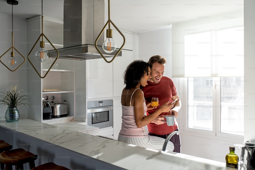 Casal inter-racial afetuoso tomando café da manhã saudável enquanto no telefone celular em casa na cozinha