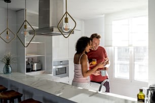 Couple interracial affectueux prenant un petit-déjeuner sain tout en étant sur le téléphone portable à la maison dans la cuisine