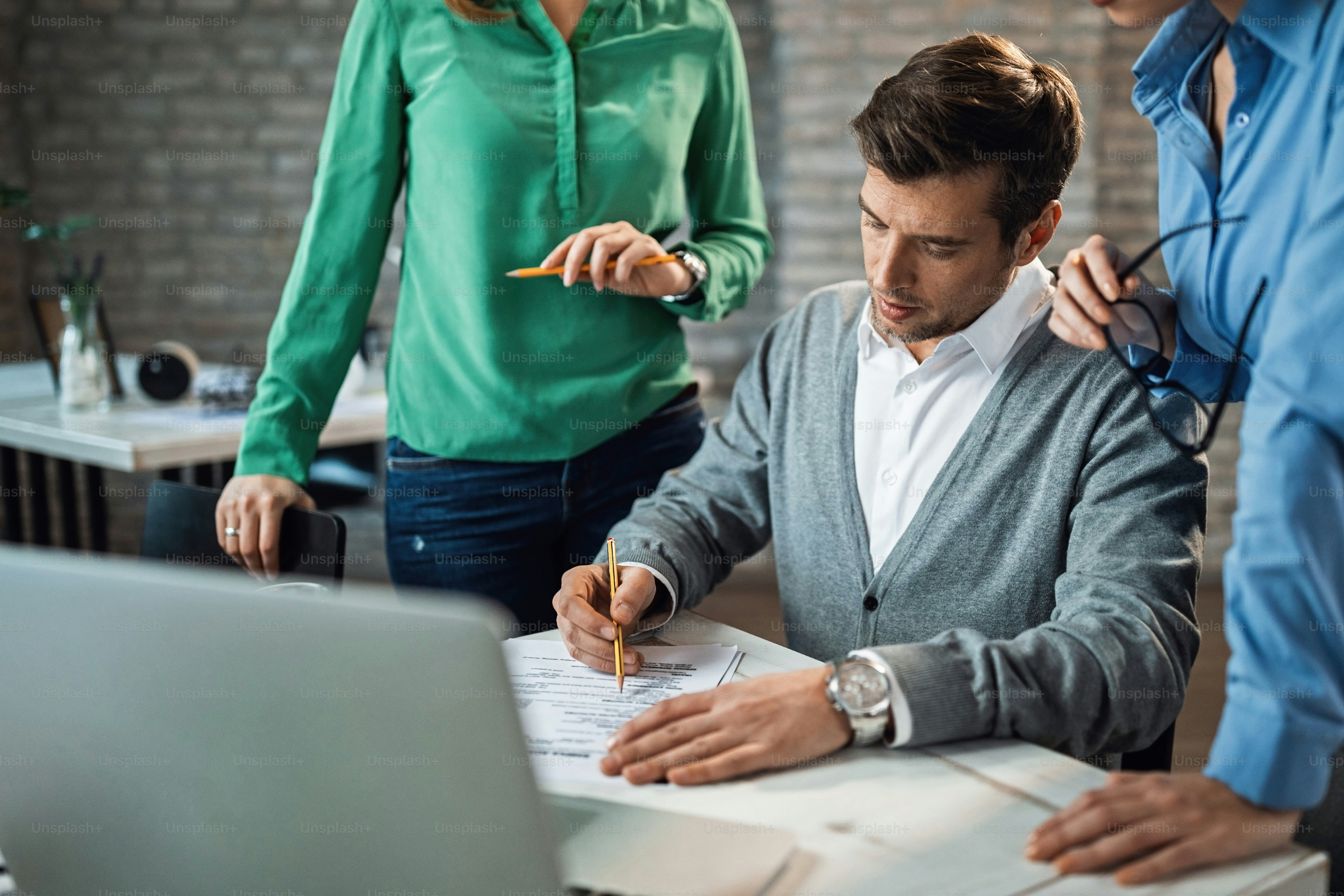 Male entrepreneur is signing a contract in presence of two female