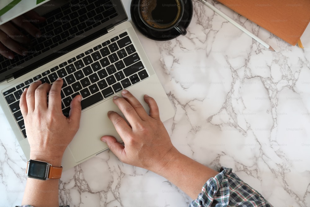 Top view of male worker typing on laptop on marble desk