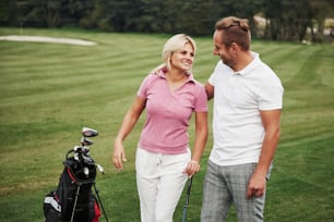 Sportive couple playing golf on a golf course, they stand to the next hole.