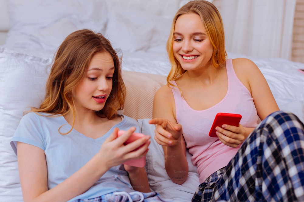 Online-Shopping. Zwei strahlende sympathische Geschwister shoppen gemeinsam online im Schlafzimmer