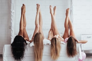 Schöne Jugend. Vier junge Frauen mit guter Körperform liegen mit hochgezogenen Beinen auf dem Bett.