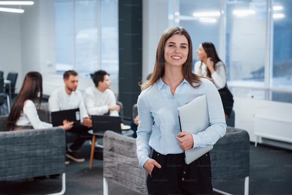 Modern startup business. Portrait of young girl stands in the office with employees at background.