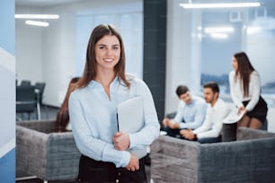 In front of business people. Portrait of young girl stands in the office with employees at background.
