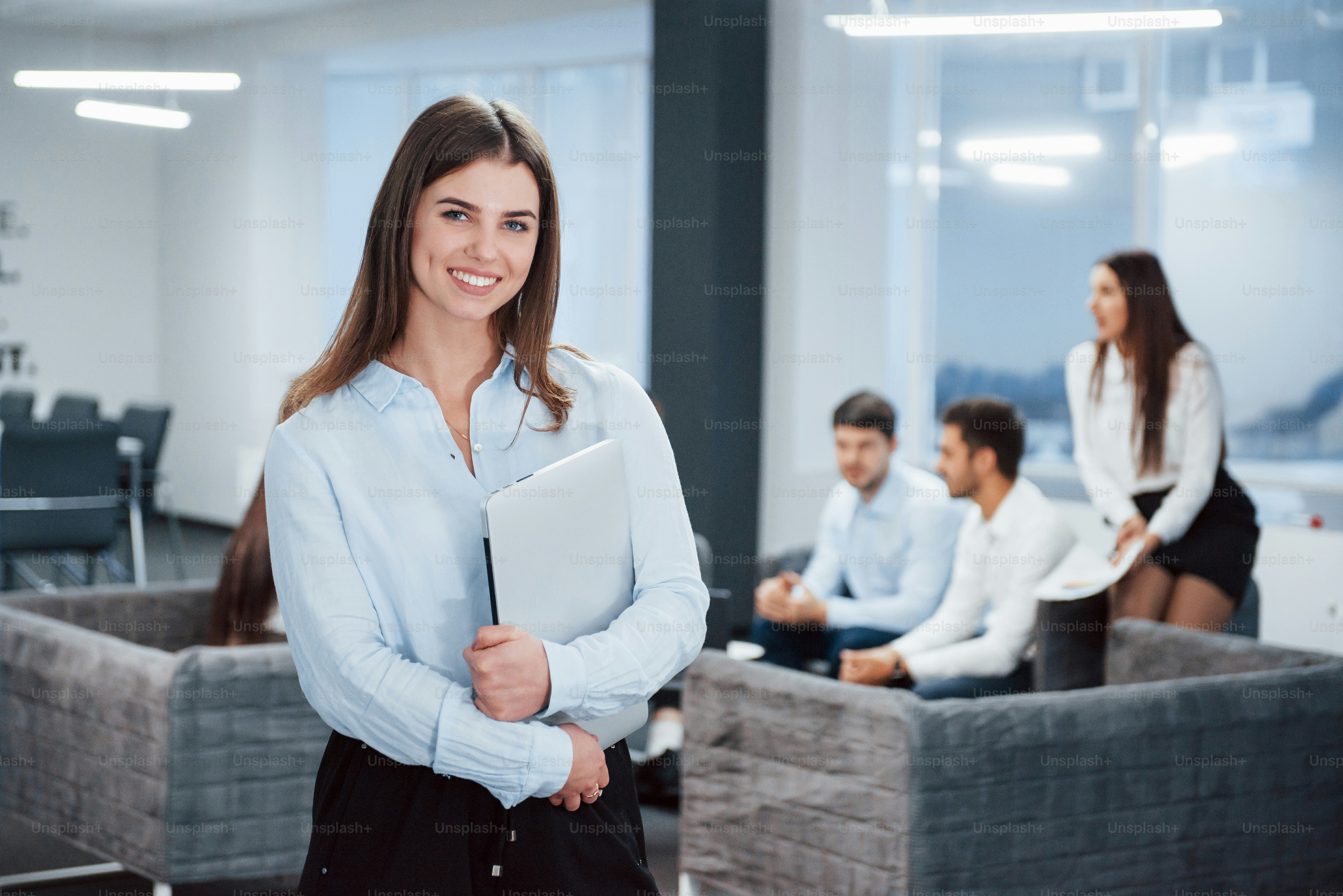 Wunderschöne Frau. Porträt eines jungen Mädchens steht im Büro mit Mitarbeitern im Hintergrund.