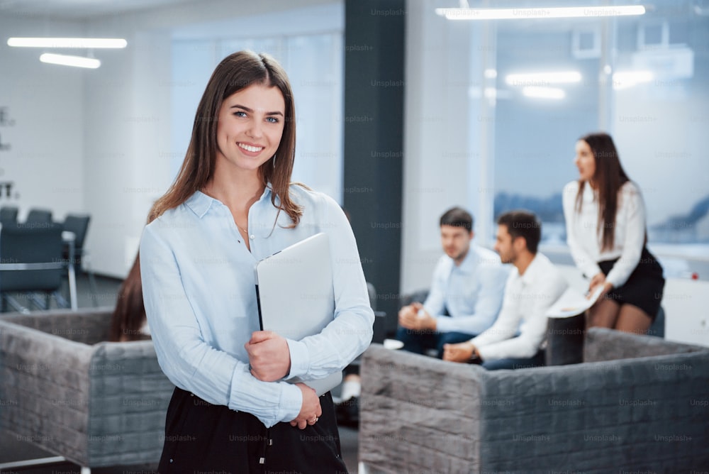 Gorgeous woman. Portrait of young girl stands in the office with employees at background.