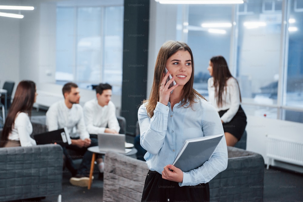 Has a deal. Portrait of young girl stands in the office with employees at background.