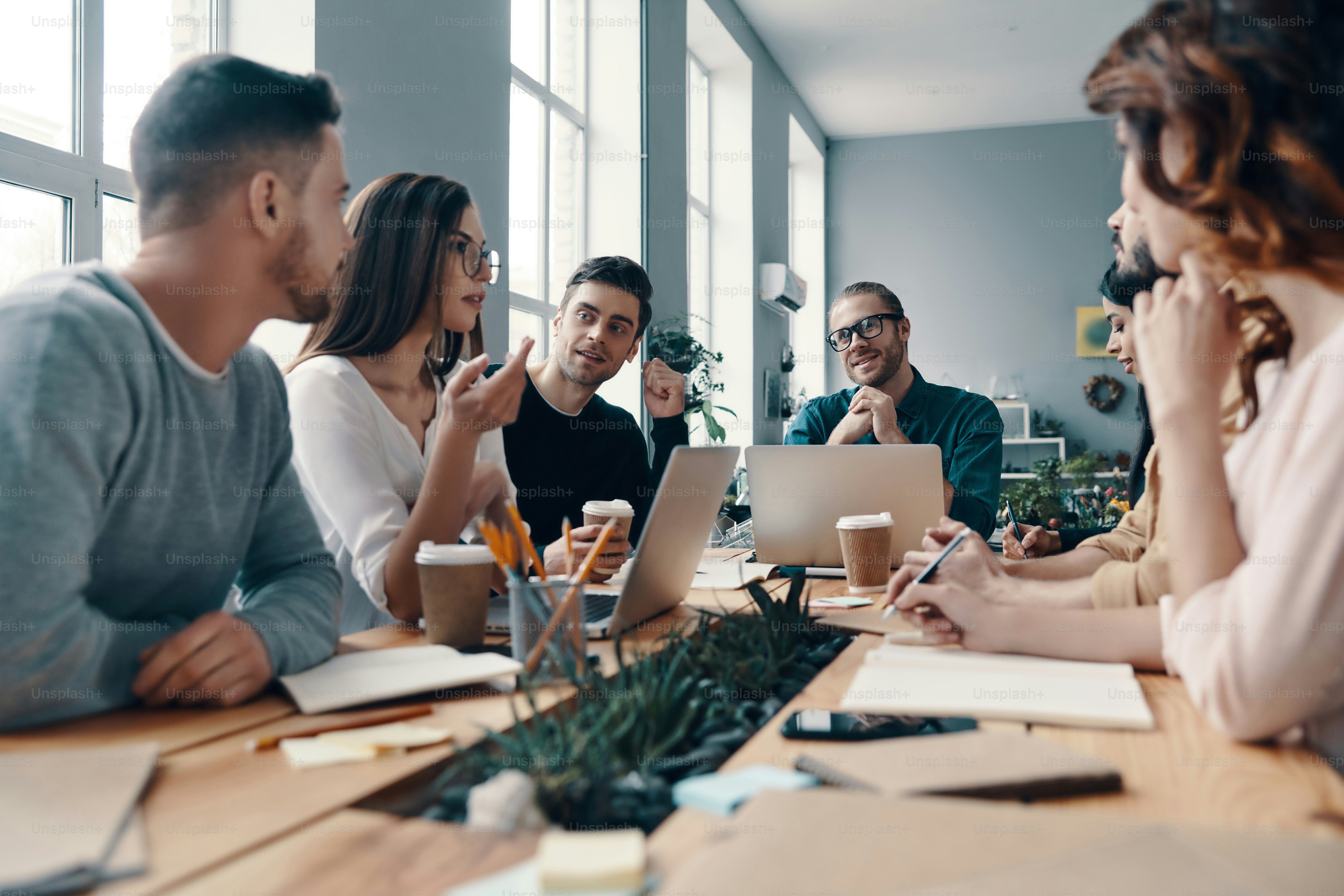 Group of young modern people in smart casual wear discussing something and smiling while working in the creative office