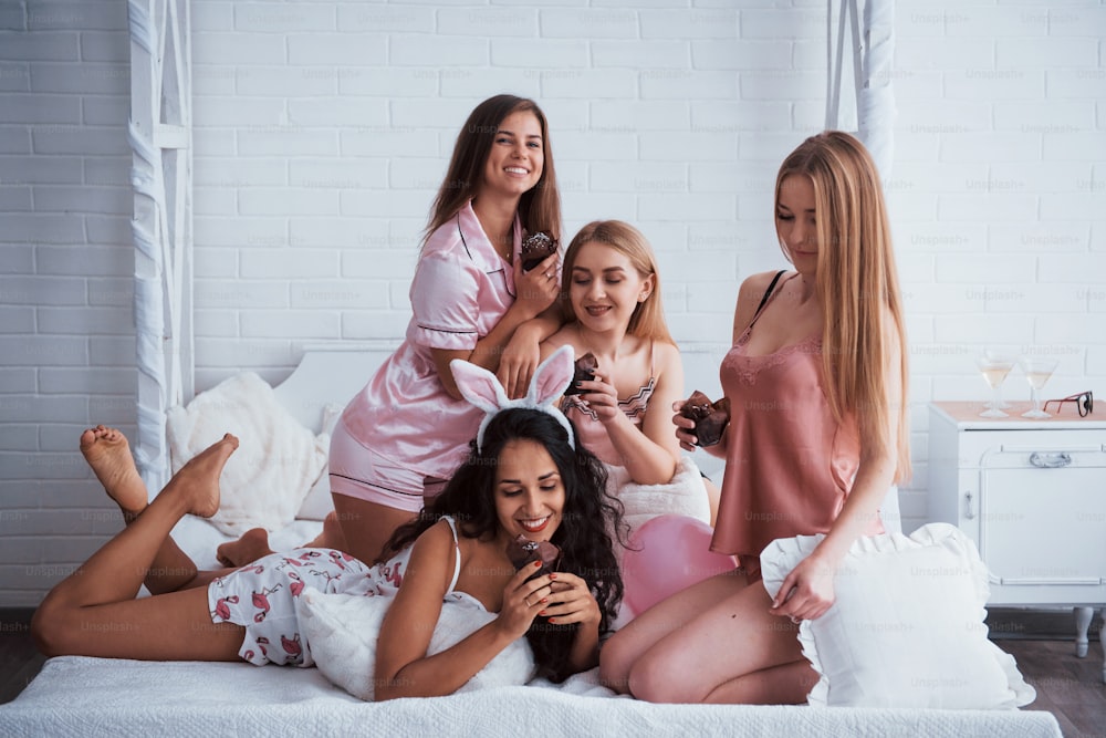 Good food creates nice mood. Cute girls have meeting and holiday in the awesome lighted room with white walls and bed. Chocolate cookies in the hands.