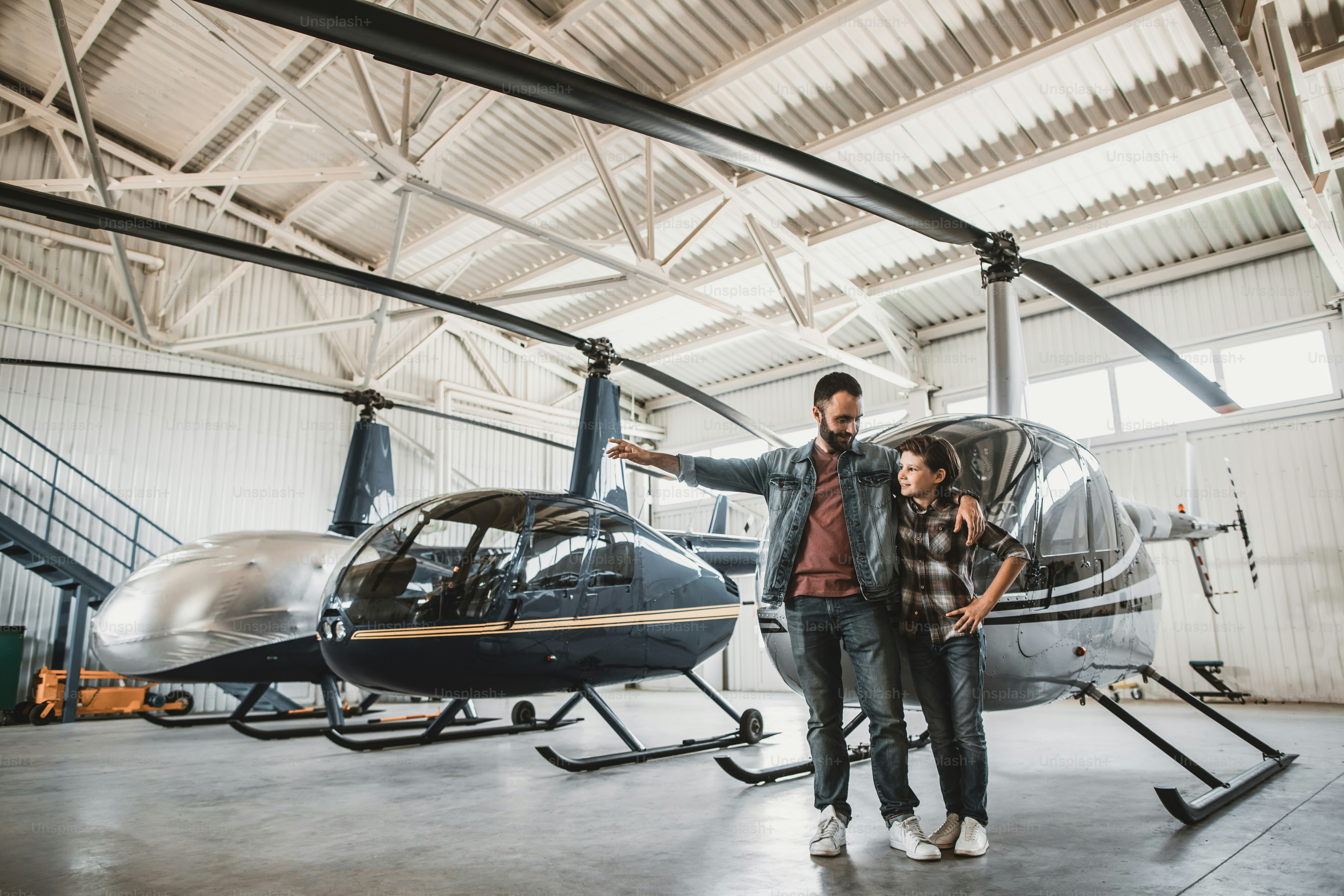 Full length happy man describing instruction for cheerful guy while gesticulating hand. He hugging child near rotor planes