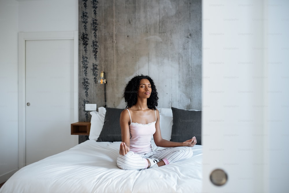 Atractiva mujer negra sentada en posición de loto en la cama meditando