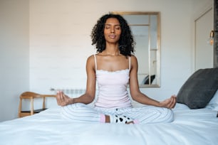 Attraente donna nera seduta in posizione di loto sul letto che medita