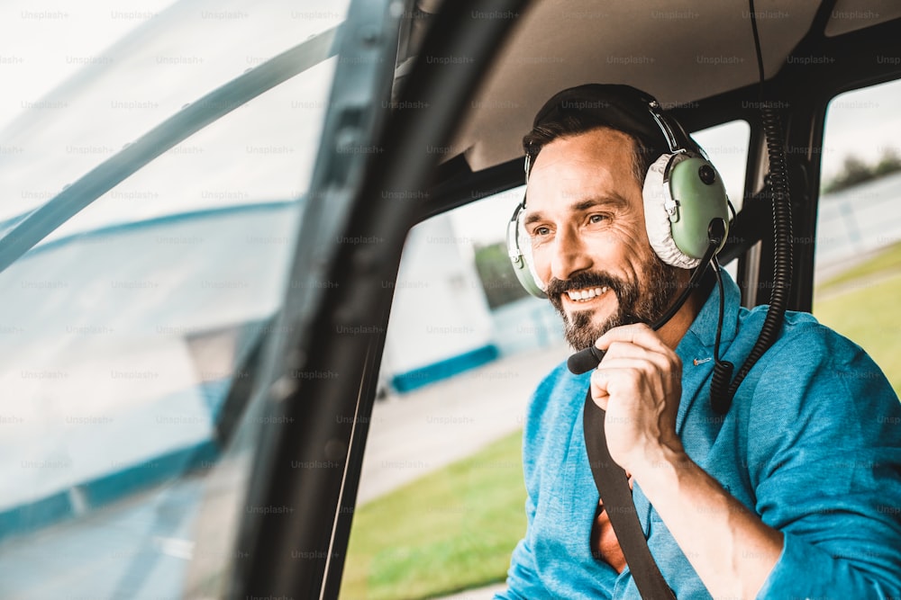 Cheerful relaxed man in big headphones smiling while sitting in the helicopter cabin