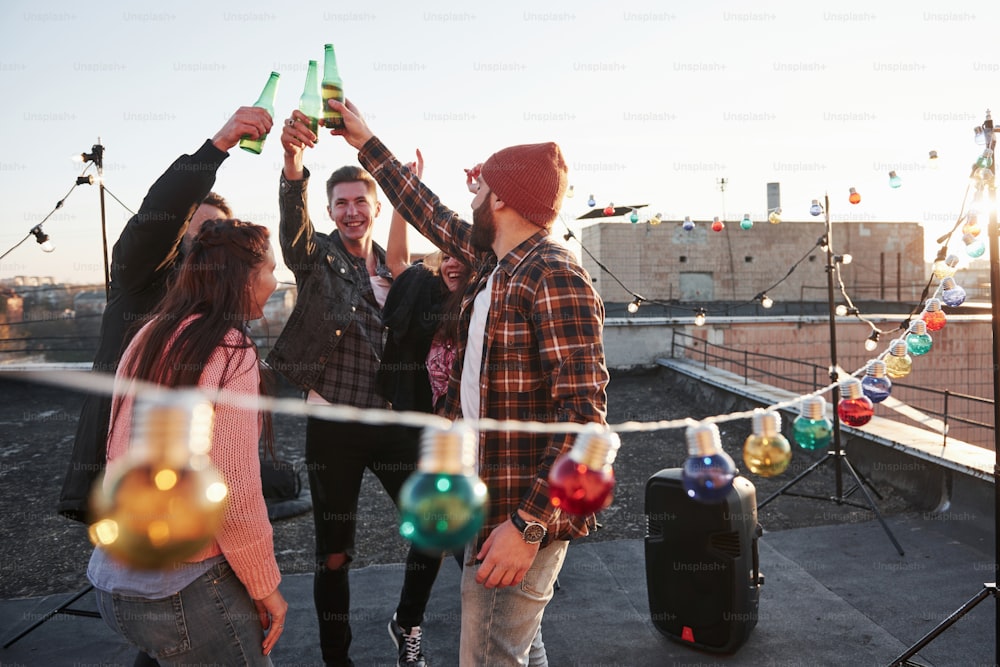 Unity of people. Holidays on the rooftop. Cheerful group of friends raised their hands up with alcohol.