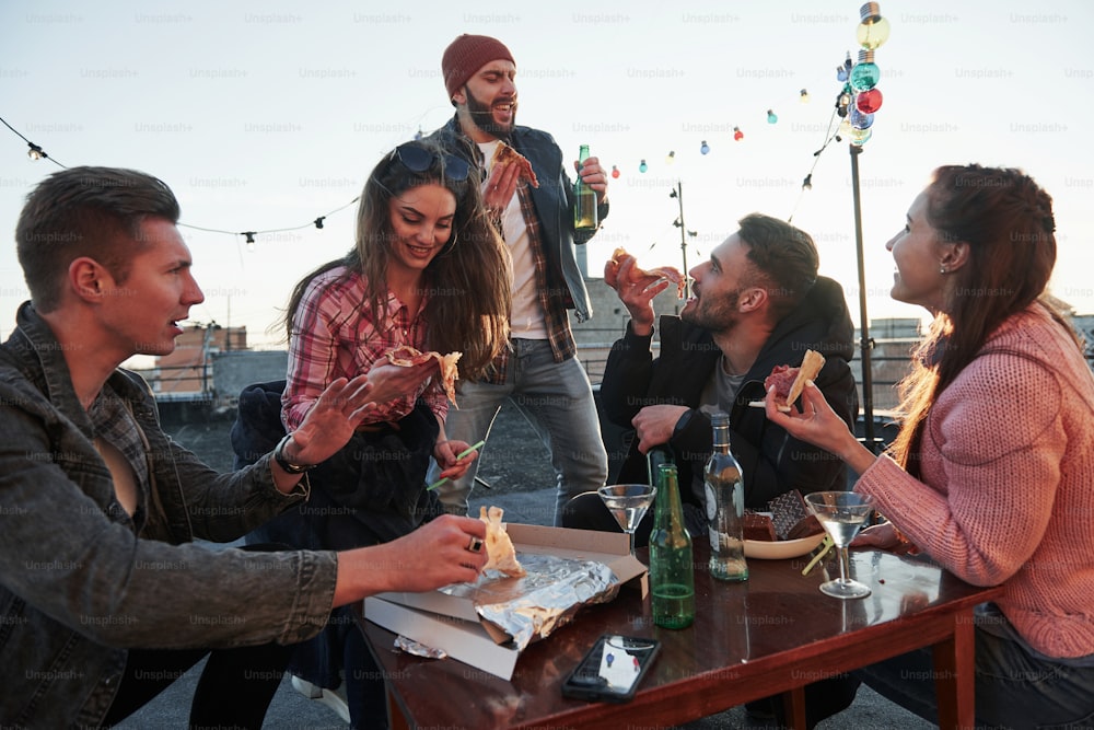 Time for singing. At least guy in red hat thinks so. Eating pizza at the rooftop party. Good friends have weekend with some delicious food and alcohol.