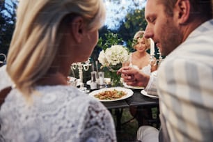 Un hombre le da ensalada a su esposa para que la pruebe. Los amigos se reúnen por la noche. Bonito restaurante al aire libre.