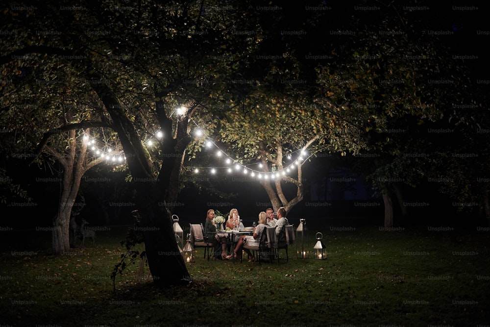 Um local isolado. À noite. Os amigos jantam no lindo lugar ao ar livre.