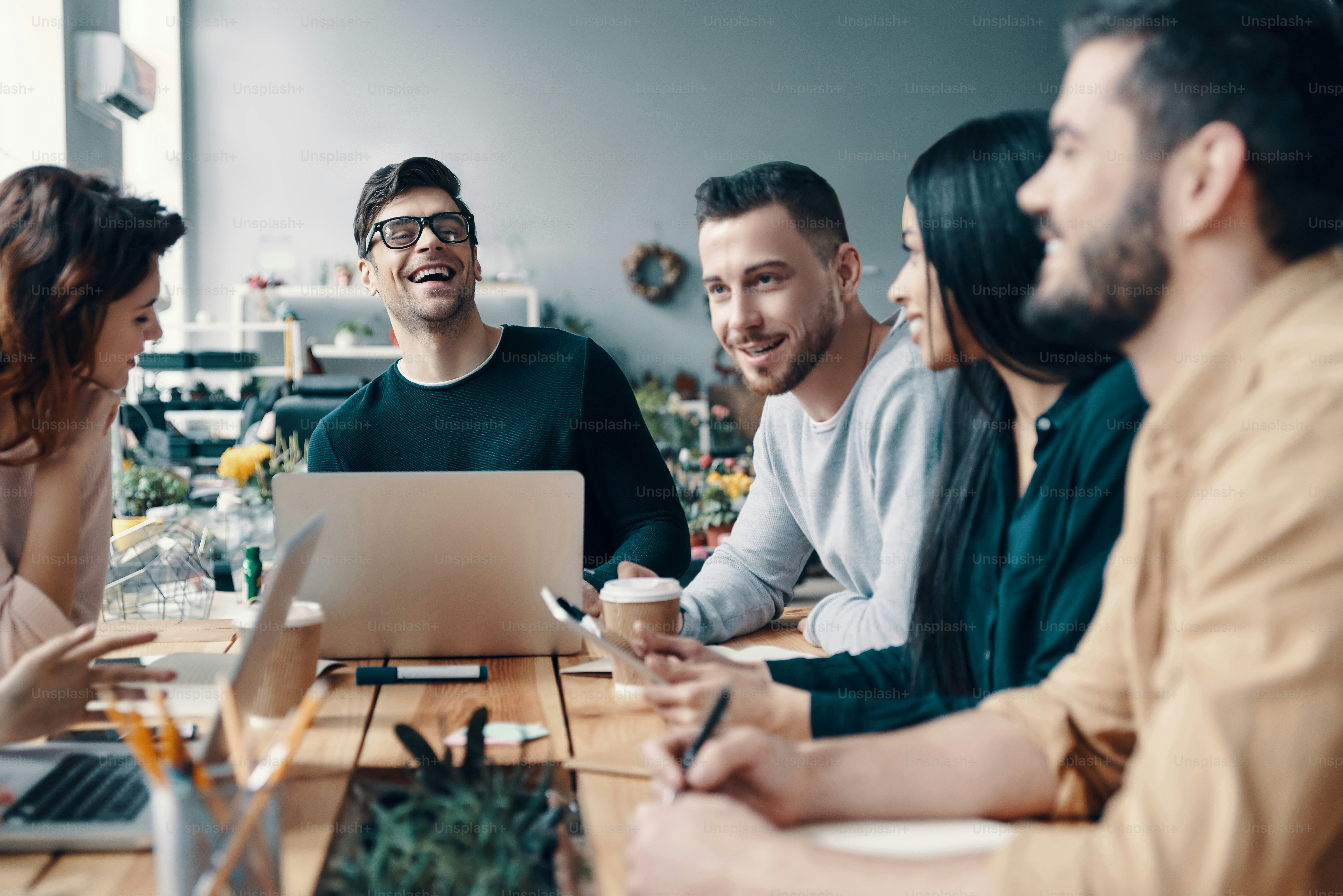 Group of young modern people in smart casual wear discussing something and smiling while working in the creative office