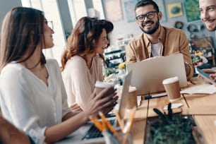 Group of young modern people in smart casual wear discussing something and smiling while working in the creative office