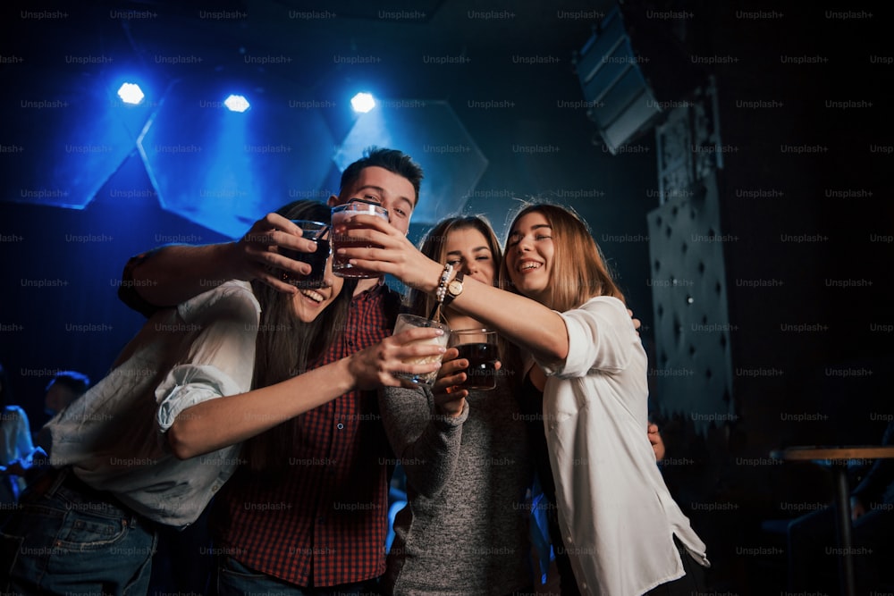 Vorderansicht. Gruppe junger Freunde, die lächeln und im Nachtclub anstoßen.