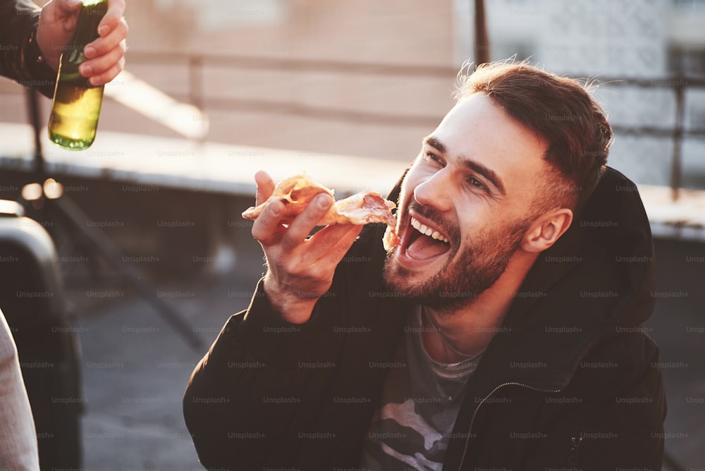 Guy eating a delicious pizza on the rooftop while having party with friends.