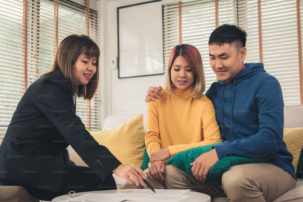 Happy young Asian couple and Real Estate Agent agent. Cheerful young man signing some documents while sitting at desk together with his wife. Buying new house real estate. Signing good condition contract.