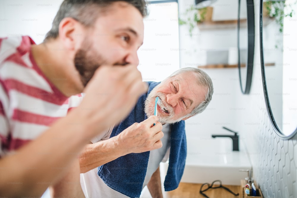 Um filho hipster adulto e um pai idoso escovando os dentes no banheiro dentro de casa.