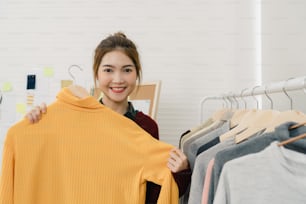 Asian female fashion designer working, checking and choosing clothes design on clothes rack while working in the fashion studio. Lifestyle beautiful professional designer women working concept.