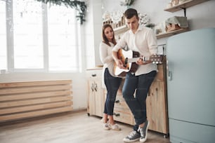 Photo in full growth. Young guitarist playing love song for his girlfriend in the kitchen.