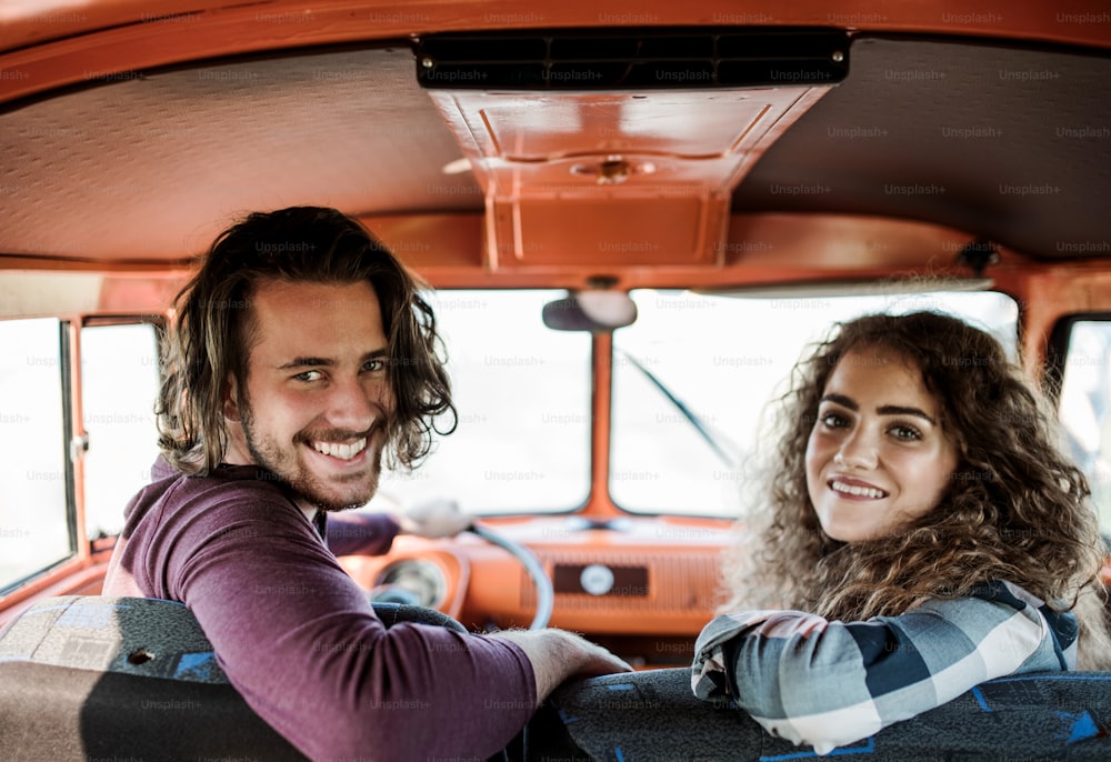 Una pareja joven en un viaje por carretera a través del campo, conduciendo una minivan retro.
