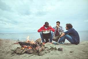 Volksthema. Drei junge Freunde verbringen Zeit am Lagerfeuer, während einer von ihnen Perkussionsmelodien komponiert