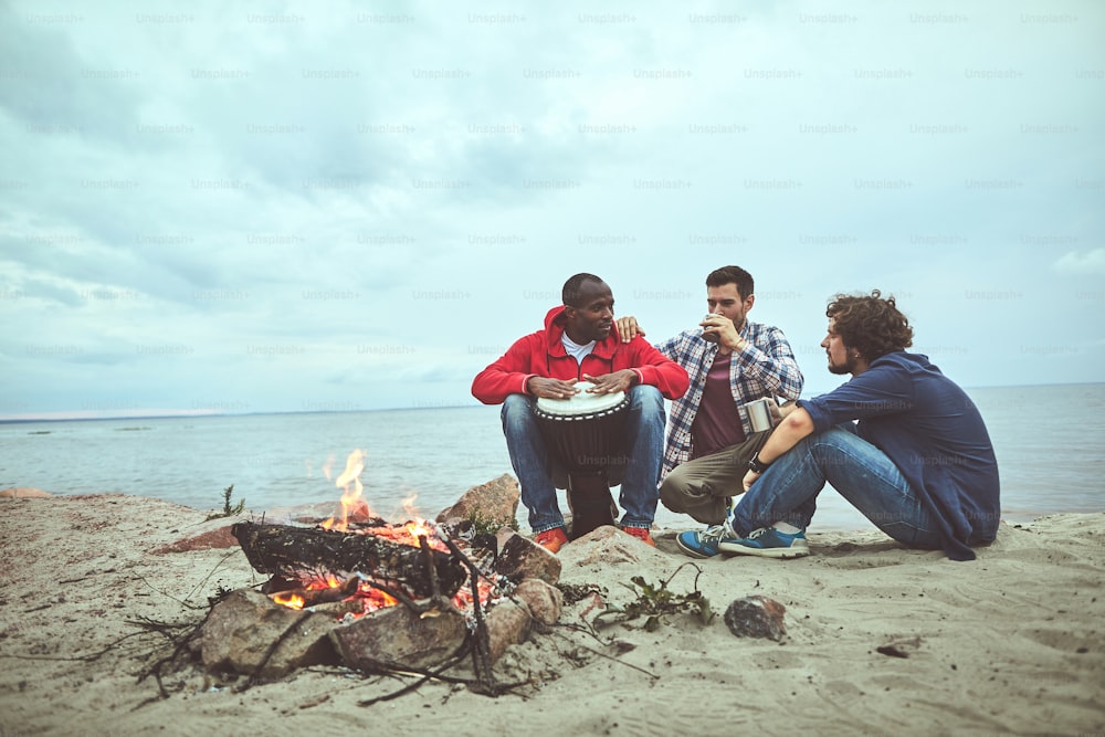 Thème folklorique. Trois jeunes amis passent du temps autour du feu de camp pendant que l’un d’eux compose des mélodies de percussions