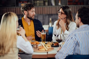 Amigos multiétnicos sentados em restaurante, bebendo álcool, conversando e comendo hambúrgueres para o jantar.