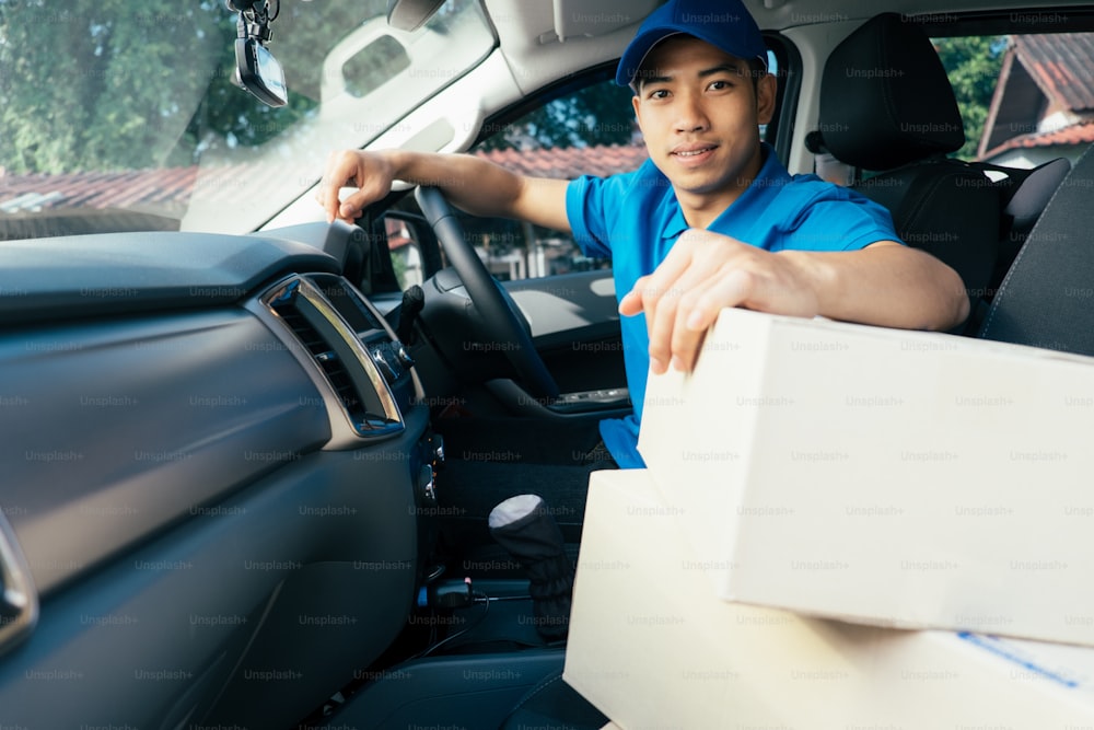 Delivery driver driving car with packages on seat outside the warehouse.