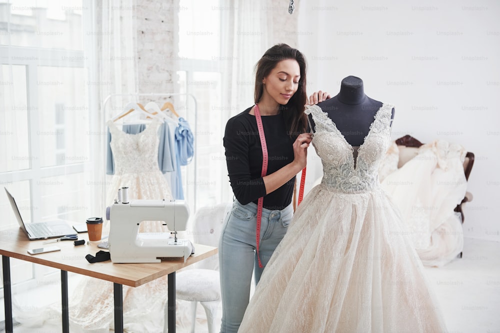 Imagina cómo se sentará en la novia. Una diseñadora de moda trabaja en la ropa nueva en el taller.