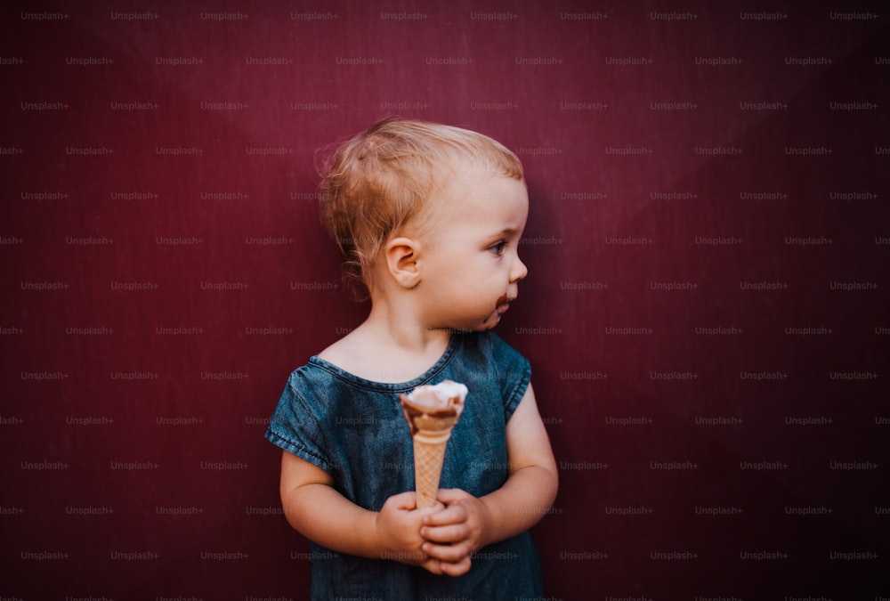 여름에 야외에서 아이스크림을 먹고 있는 귀여운 작은 유아 소녀의 전면 모습.