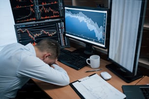 Cansado de dia duro. Homem trabalhando on-line no escritório com várias telas de computador em gráficos de índice.