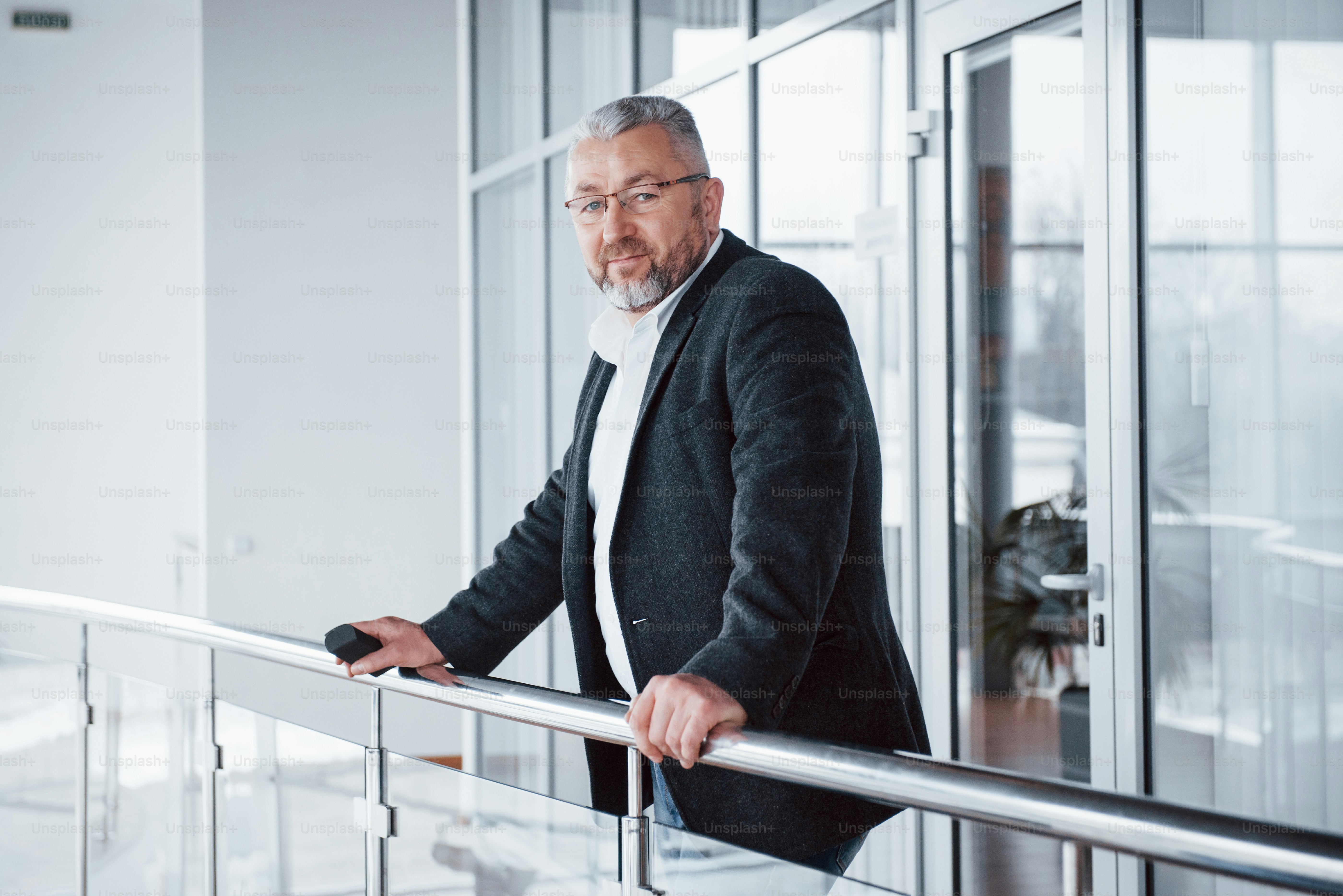 Looking into the camera. Man in classic wear stands in modern building and leaned on the railing