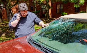 Motorista, homem fazendo telefonema após acidente de carro com para-brisa quebrado