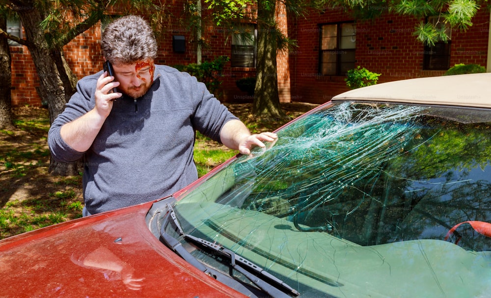 Fahrer, Mann, der nach Autounfall mit zerbrochener Windschutzscheibe telefoniert