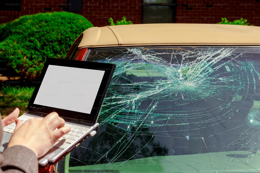Agente de seguros que completa el formulario de reclamo de seguro en una computadora portátil después de un accidente de parabrisas