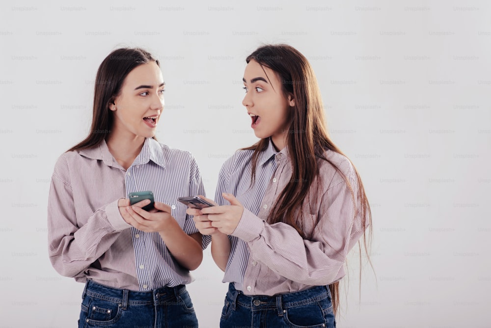 Esta última noticia es increíble. Dos hermanas gemelas de pie y posando en el estudio con fondo blanco.