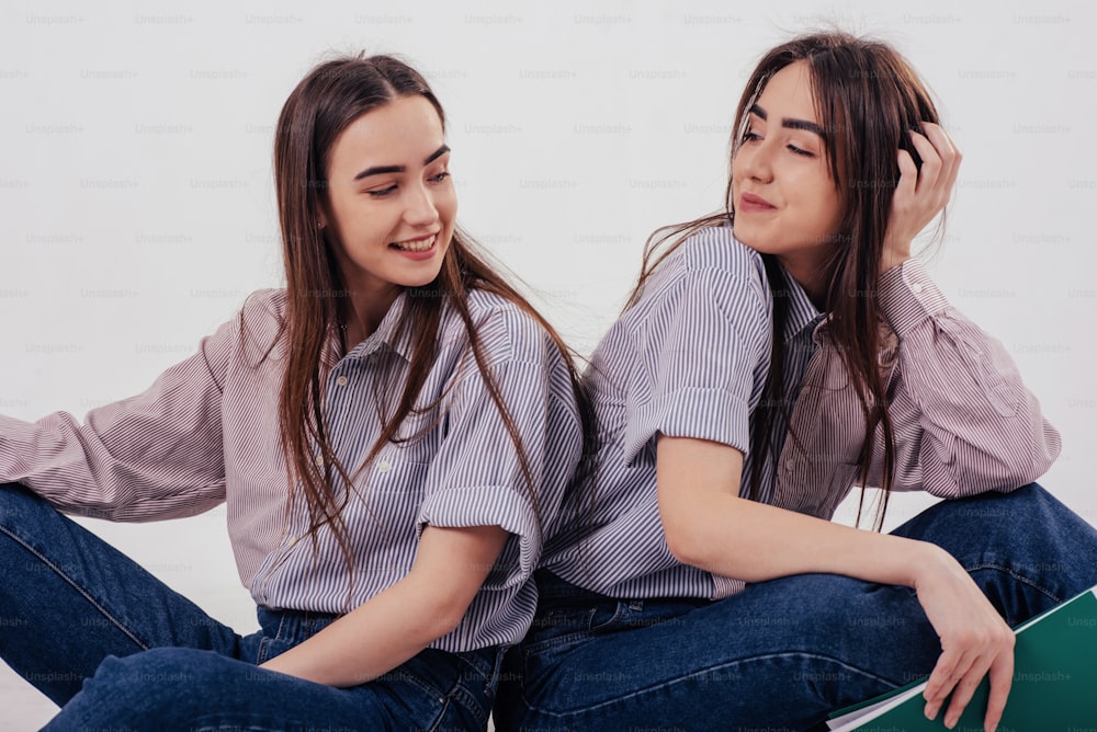 아름다운 소녀들. 두 자매 쌍둥이가 흰색 배경의 스튜디오에 앉아 포즈를 취하고 있다.