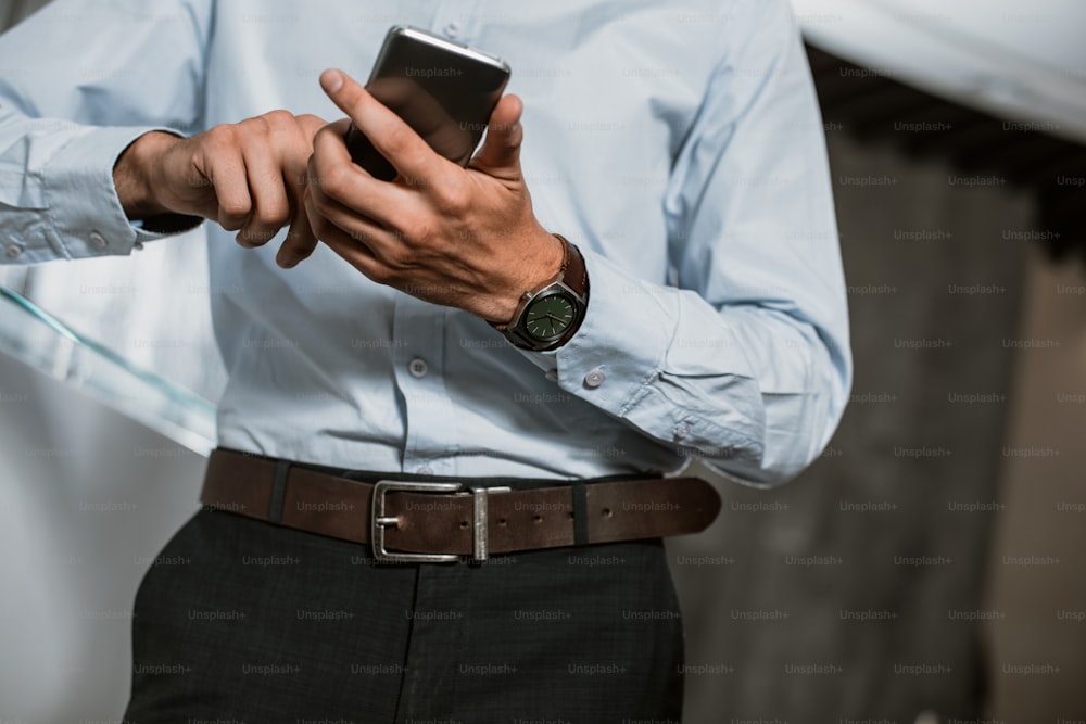 Primer plano de ángulo bajo de manos masculinas usando un teléfono inteligente. Un hombre con ropa de oficina está de pie y sosteniendo un dispositivo. Está escribiendo en la pantalla táctil