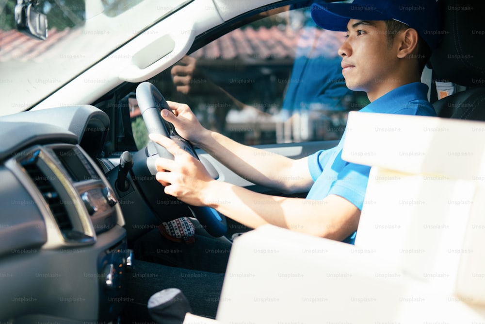 Delivery driver driving car with packages on seat outside the warehouse.