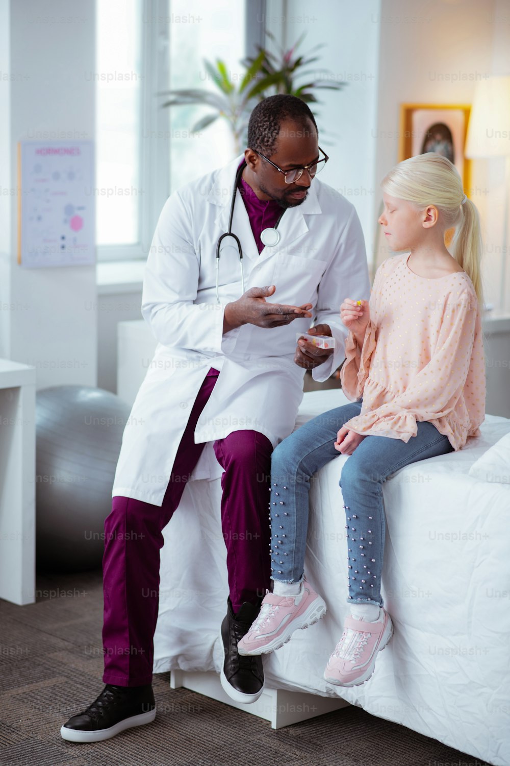 Sitting near doctor. Blonde-haired stylish girl wearing jeans and pink blouse sitting near doctor